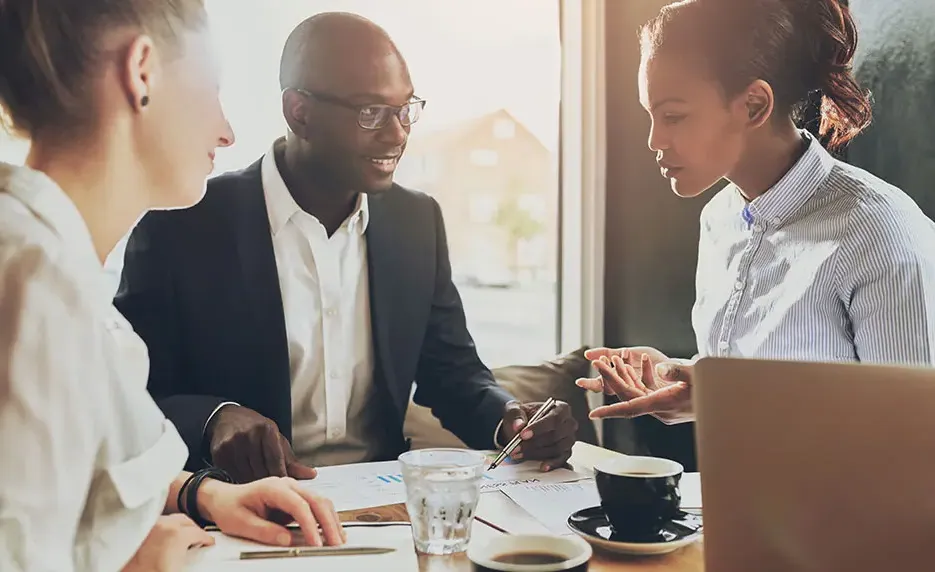 Three business people discuss the data listed on papers in front of them